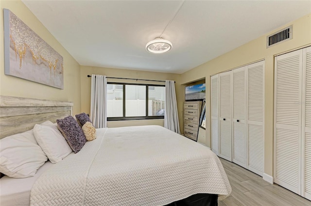 bedroom featuring multiple closets, visible vents, and light wood finished floors