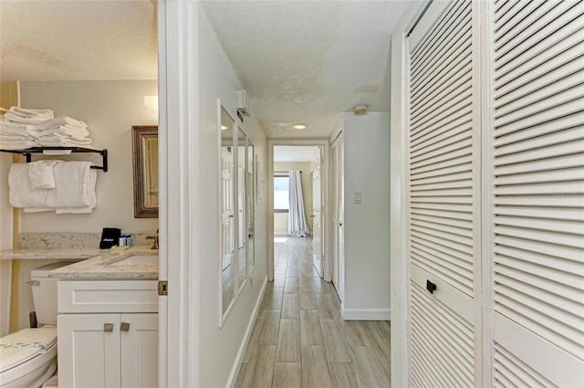 hall with light wood-type flooring, a sink, a textured ceiling, and baseboards