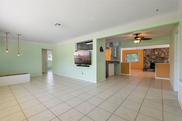 unfurnished living room featuring visible vents, ceiling fan, a stone fireplace, light tile patterned flooring, and a textured ceiling