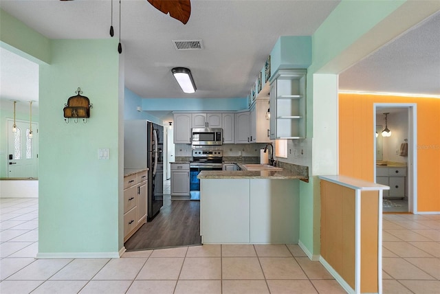 kitchen featuring visible vents, a sink, stainless steel appliances, a peninsula, and light tile patterned flooring