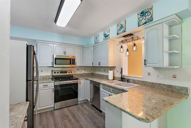 kitchen featuring wood finished floors, a peninsula, open shelves, a sink, and stainless steel appliances