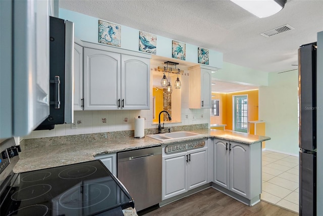 kitchen featuring visible vents, backsplash, appliances with stainless steel finishes, a peninsula, and a sink