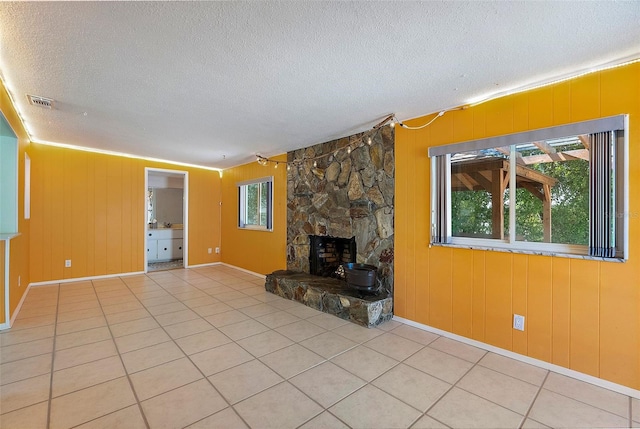 unfurnished living room with a stone fireplace, visible vents, tile patterned flooring, and a textured ceiling