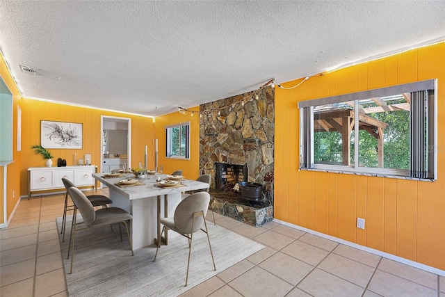 dining room featuring light tile patterned floors, visible vents, a textured ceiling, and a stone fireplace