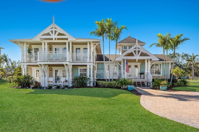 view of front facade with a front yard, a balcony, french doors, and covered porch