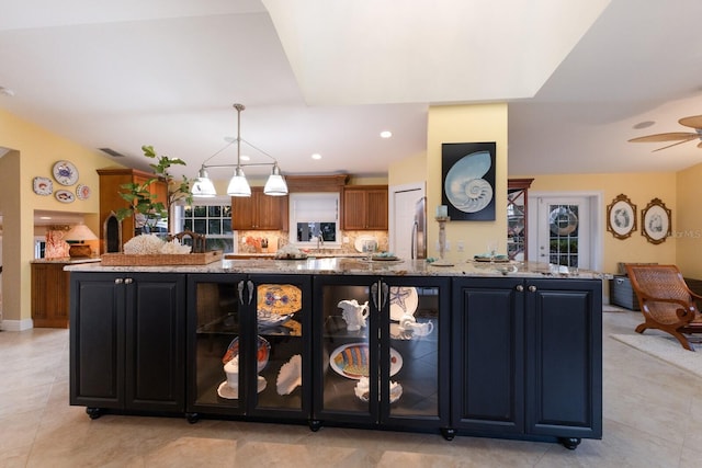 kitchen with decorative light fixtures, light stone countertops, a ceiling fan, and backsplash