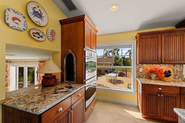 kitchen with stainless steel double oven, visible vents, light stone countertops, and a healthy amount of sunlight