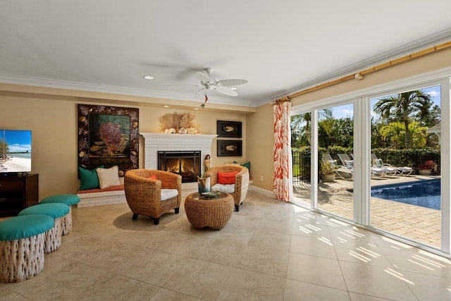 living area with a ceiling fan, baseboards, a fireplace, crown molding, and tile patterned floors