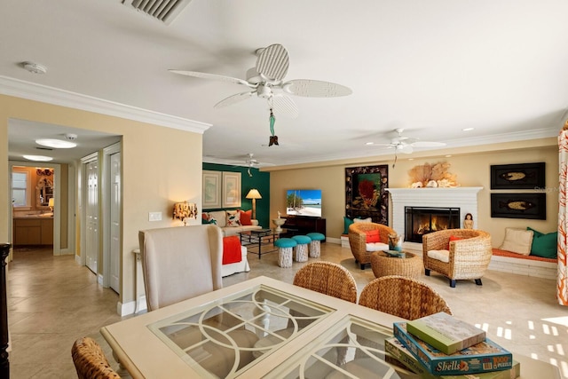 interior space with a ceiling fan, baseboards, visible vents, a warm lit fireplace, and ornamental molding