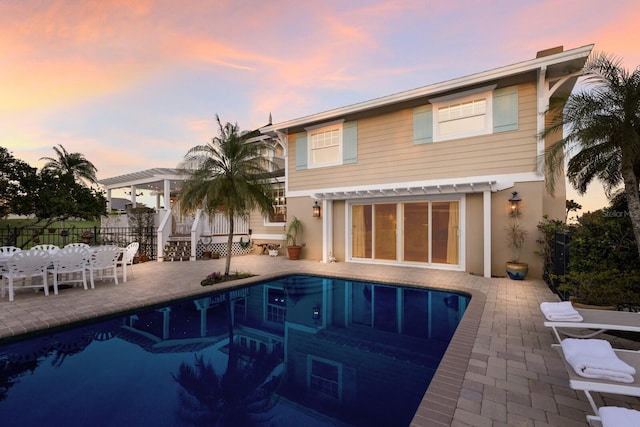 back of property at dusk with a fenced in pool, fence, stucco siding, a pergola, and a patio