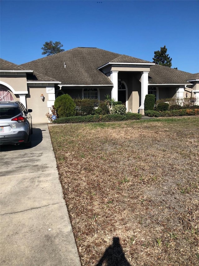 ranch-style home with stucco siding, roof with shingles, and a front yard