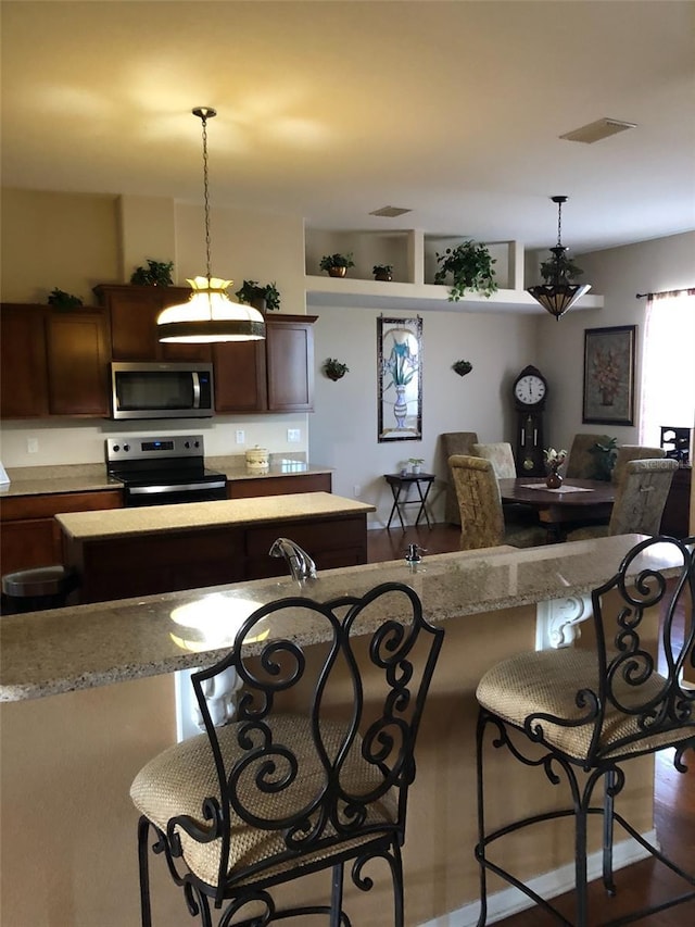 kitchen with hanging light fixtures, visible vents, appliances with stainless steel finishes, and a breakfast bar area