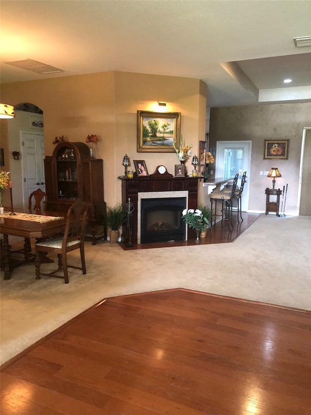 carpeted living area featuring a fireplace with flush hearth, wood finished floors, and visible vents