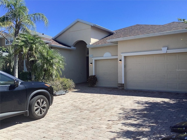 ranch-style house featuring a shingled roof, decorative driveway, an attached garage, and stucco siding