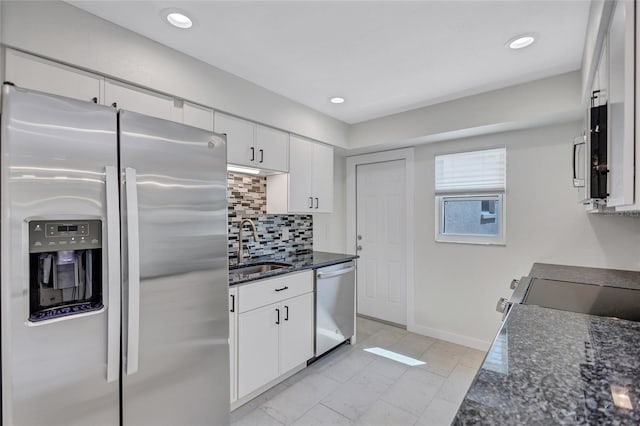 kitchen with a sink, dark stone countertops, stainless steel appliances, white cabinets, and decorative backsplash