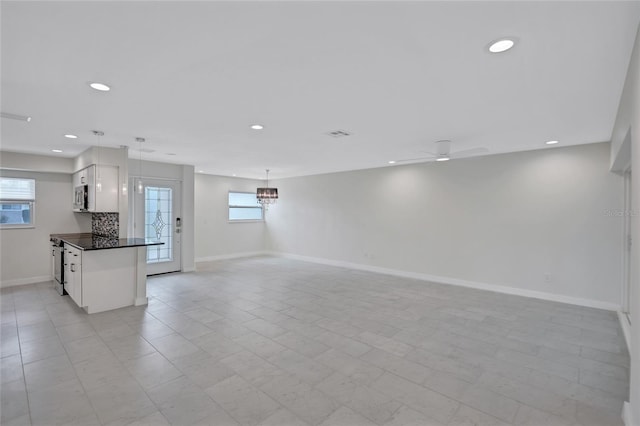 unfurnished living room with recessed lighting, a healthy amount of sunlight, and baseboards