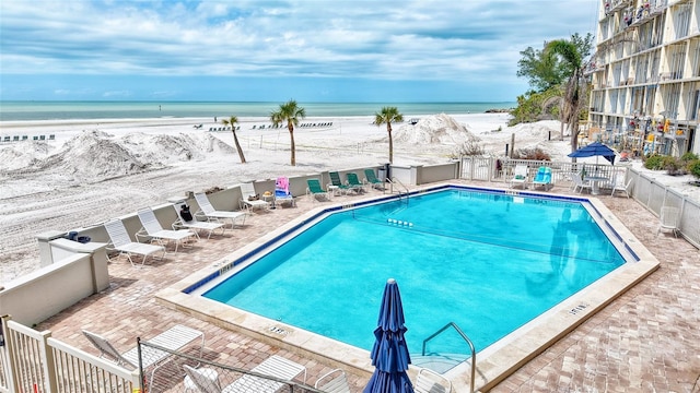 community pool with a patio area, a beach view, a water view, and fence