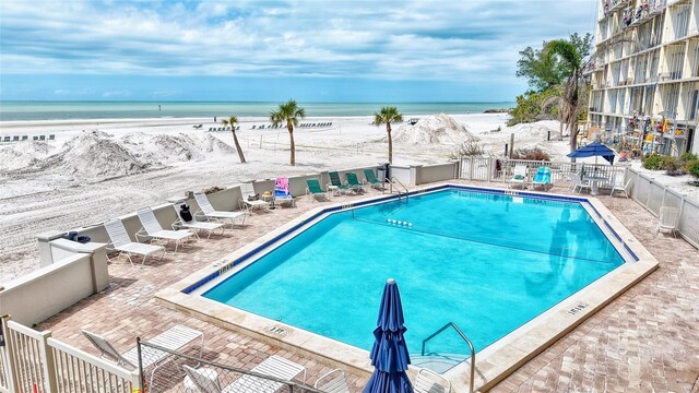 community pool with a patio area, a beach view, a water view, and fence