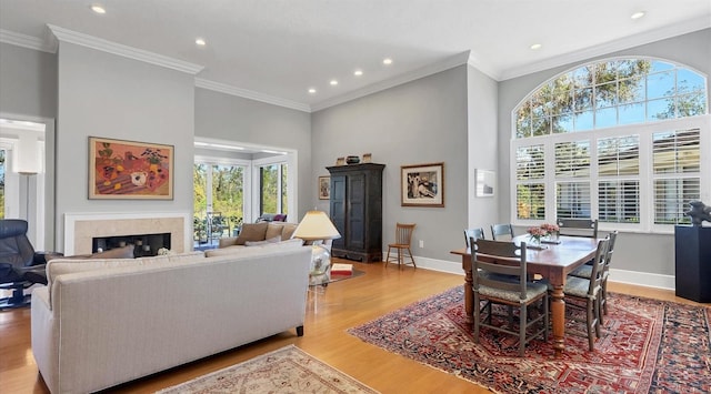 living area featuring crown molding, recessed lighting, light wood-style floors, a glass covered fireplace, and baseboards