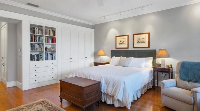 bedroom featuring wood finished floors, visible vents, a ceiling fan, ornamental molding, and a closet