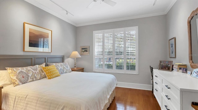 bedroom featuring rail lighting, baseboards, ornamental molding, and dark wood-type flooring