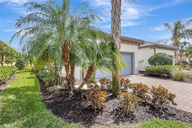 view of property exterior with decorative driveway, stucco siding, a lawn, an attached garage, and a tiled roof