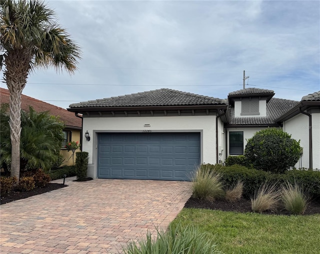 view of front of home with a tiled roof, decorative driveway, a garage, and stucco siding