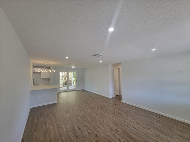 unfurnished living room featuring a textured ceiling, recessed lighting, dark wood-style flooring, visible vents, and baseboards