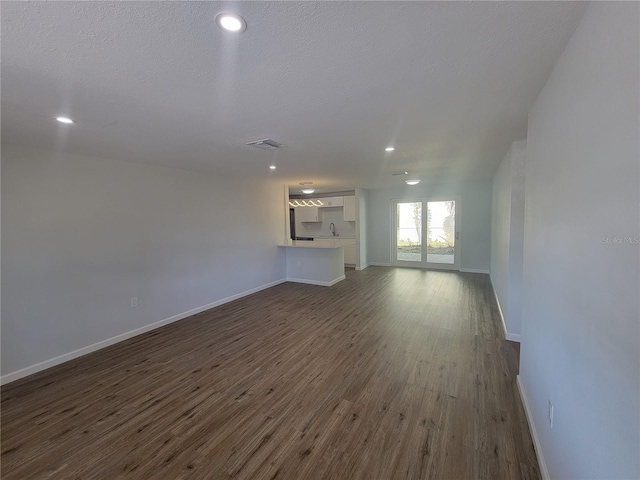 unfurnished living room with dark wood-type flooring, visible vents, a textured ceiling, and baseboards