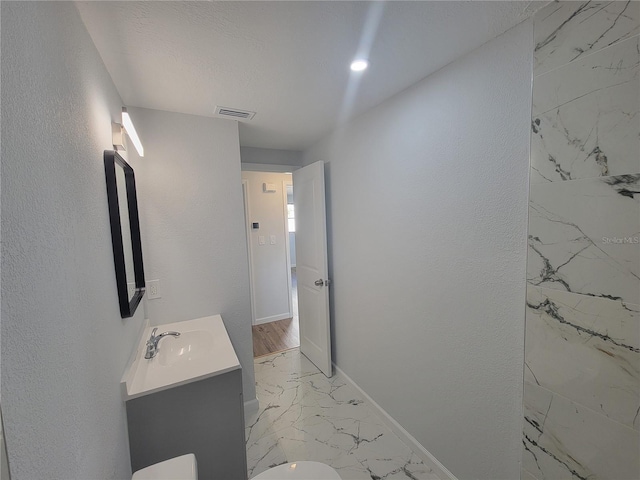 bathroom with marble finish floor, visible vents, a textured wall, vanity, and baseboards