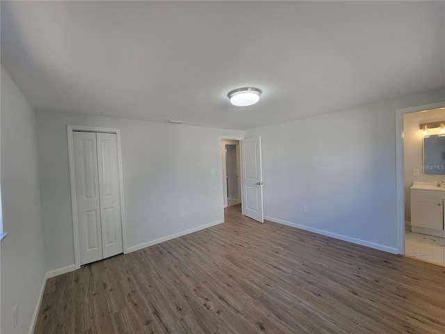 unfurnished bedroom with a closet, ensuite bathroom, baseboards, and wood finished floors