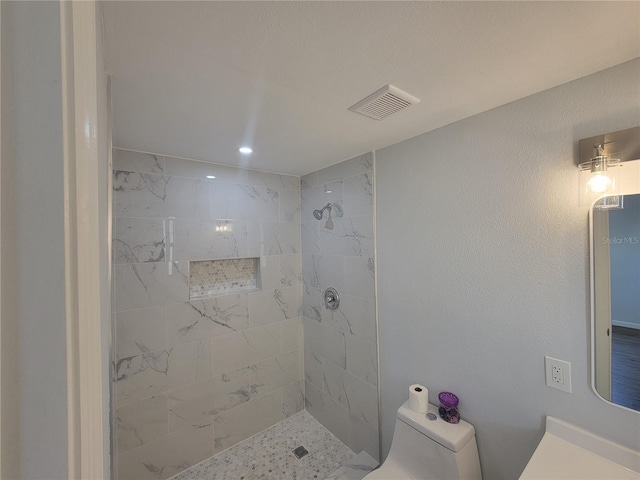 bathroom featuring visible vents, toilet, and tiled shower