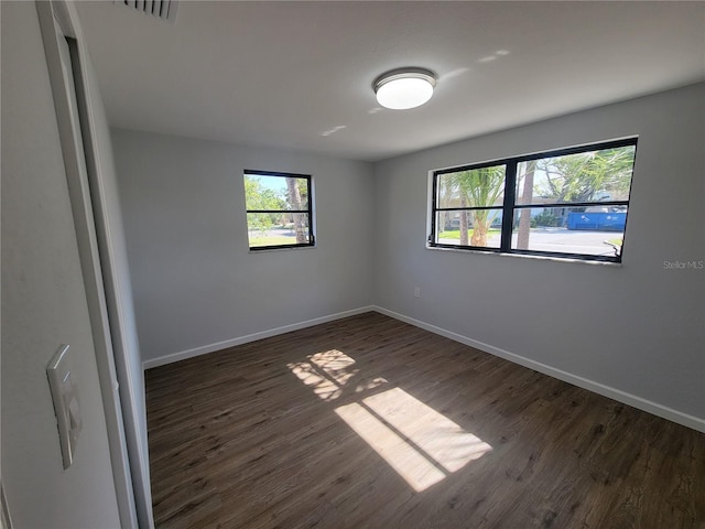 unfurnished room featuring visible vents, baseboards, and dark wood-style flooring