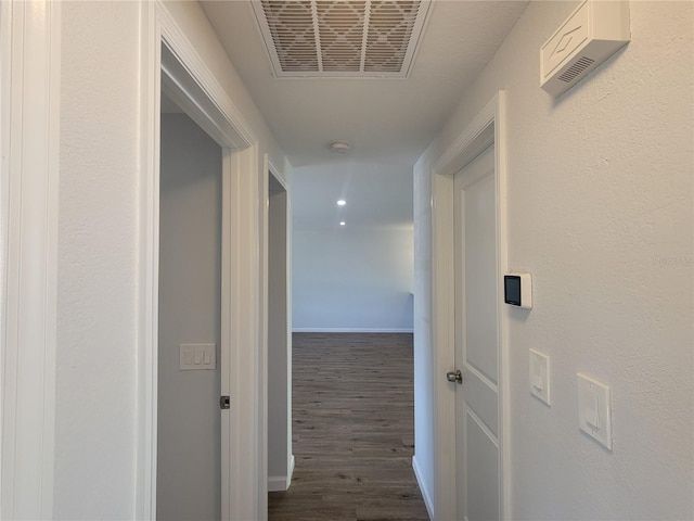 hallway with dark wood-type flooring, visible vents, and baseboards