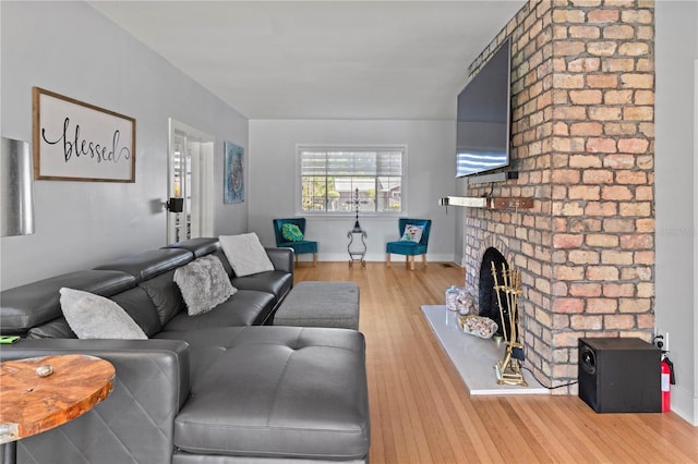 living room with a brick fireplace, baseboards, and wood finished floors