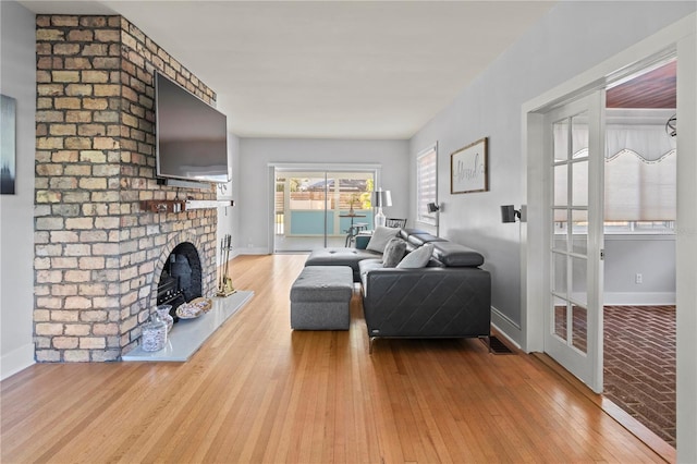 living room with baseboards, wood-type flooring, and a brick fireplace