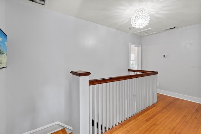 hall featuring visible vents, an upstairs landing, baseboards, wood-type flooring, and attic access