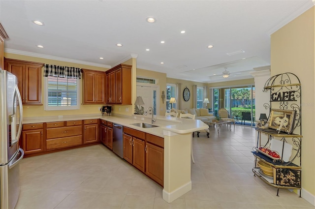 kitchen featuring a peninsula, a sink, open floor plan, appliances with stainless steel finishes, and ornamental molding