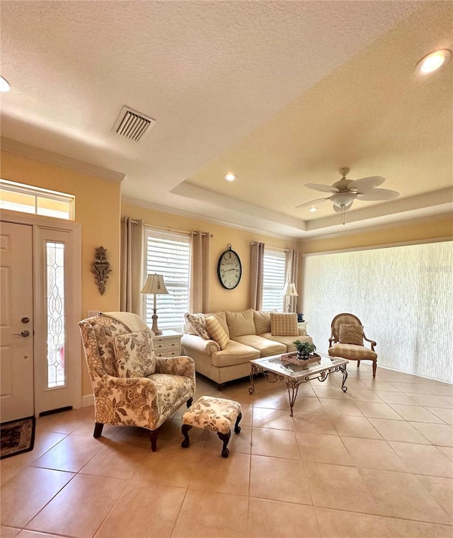 living area with light tile patterned floors, a textured ceiling, visible vents, ornamental molding, and a tray ceiling