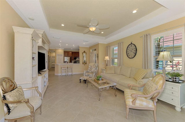 living room featuring ceiling fan, a tray ceiling, light tile patterned flooring, and crown molding