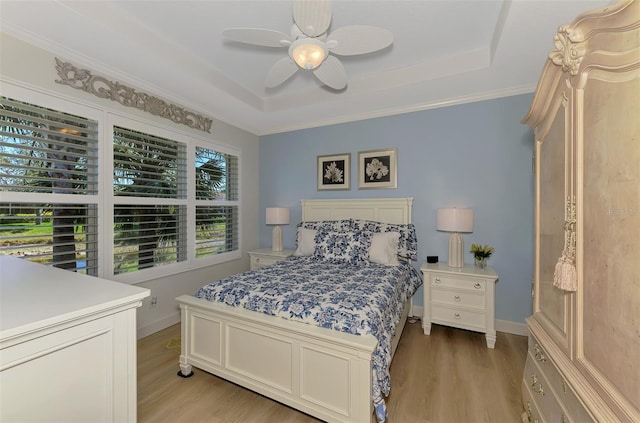 bedroom featuring a raised ceiling, light wood-style flooring, and baseboards