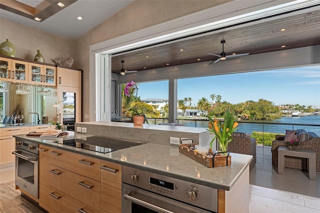 kitchen with a kitchen island, light stone counters, oven, a water view, and black electric cooktop