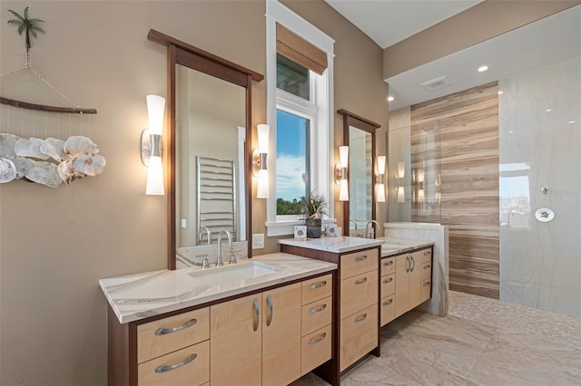 full bath with marble finish floor, walk in shower, two vanities, and a sink