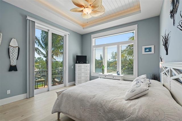 bedroom featuring light wood-style floors, baseboards, access to exterior, and a tray ceiling