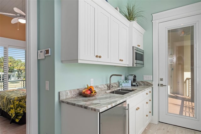 kitchen featuring light stone counters, stainless steel microwave, white cabinets, a sink, and fridge