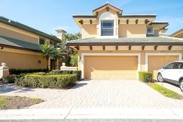 view of front of home with decorative driveway, an attached garage, a tile roof, and stucco siding