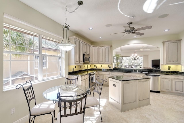 kitchen featuring arched walkways, a kitchen island, appliances with stainless steel finishes, decorative light fixtures, and a sink