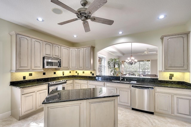 kitchen with arched walkways, backsplash, appliances with stainless steel finishes, a sink, and dark stone counters