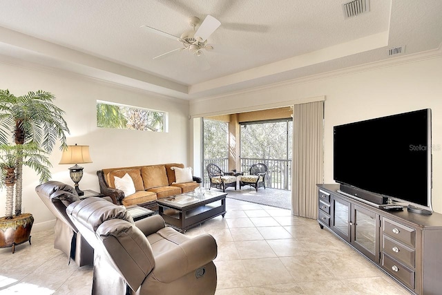 living area with a ceiling fan, visible vents, a raised ceiling, and a textured ceiling