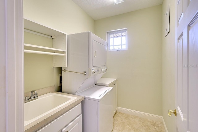 laundry room with light tile patterned flooring, a sink, baseboards, cabinet space, and stacked washer and clothes dryer